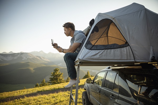 man texting from his tent on top of a car