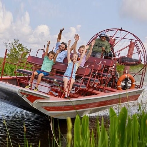 family of four with arms in the air enjoying a ride on a Lousiana air boat gliding in the swamp